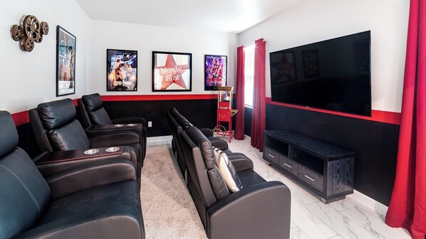 A home theater room with black leather recliners, a large flat-screen TV, and movie posters on the wall.