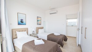 A hotel room with two beds, a window, an air conditioning unit, and artwork on the walls. - Your Beautiful Holiday Villa in Protaras and Close to the Beach, Protaras Villa 1567 (Paralimni)