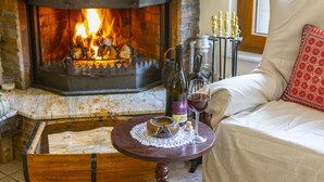 A cozy living room with a stone fireplace, a wooden coffee table with a bottle of wine and a glass, and a comfortable sofa with a red pillow. - You and Your Family Will Love This Villa Close to the Beautiful Town of Limassol, Limassol Villa 1003 (Kato Amiantos)