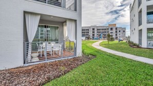 A modern apartment building with a balcony, a grassy lawn, and a pathway.