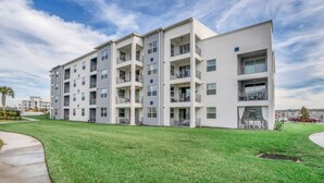 A multi-story residential building with balconies, a flat roof, and a well-maintained lawn.