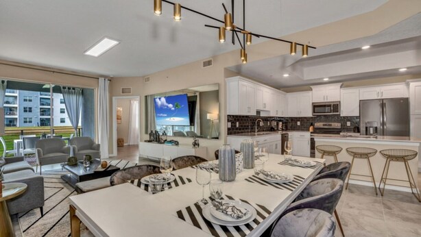 A modern kitchen with white cabinets, stainless steel appliances, and a dining area with striped table runners and grey upholstered chairs.