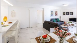 A modern living room with a grey sofa, a flat-screen TV, and a dining area with a white table and chairs. - The Perfect Holiday Apartment Minutes From the Beach in Larnaca, Larnaca Apartment 1401 (Larnaca)
