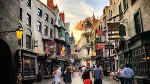 Escena callejera vibrante con edificios históricos, una estatua de dragón y una multitud de gente.