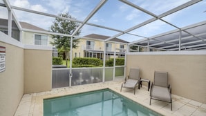 Ein überdachter Pool im Freien mit Glasverkleidung, zwei Liegestühle und Blick auf ein Wohngebäude im Hintergrund.