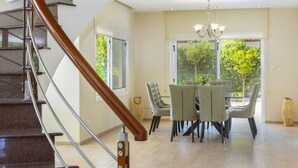Un comedor espacioso con una lámpara moderna, una mesa de comedor rodeada de sillas y una escalera con barandillas de madera que conduce a un piso superior.