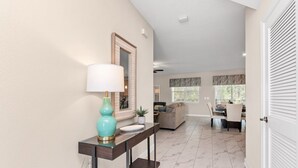 A hallway with a console table, a lamp, and a mirror. There is a dining area with a table and chairs in the background. - Your Beautiful 5 Star Villa Minutes From Disney on the Prestigious Storey Lake Resort, Orlando Villa 3653 (Kissimmee)