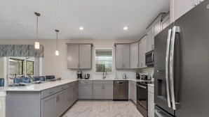 A modern kitchen with grey cabinets, stainless steel appliances, and a marble floor. - Your Beautiful 5 Star Villa Minutes From Disney on the Prestigious Storey Lake Resort, Orlando Villa 3653 (Kissimmee)