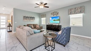 A living room with a sectional sofa, a patterned armchair, a TV, and a ceiling fan. - Your Beautiful 5 Star Villa Minutes From Disney on the Prestigious Storey Lake Resort, Orlando Villa 3653 (Kissimmee)