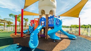 A playground with slides and climbing structures, surrounded by a fence and palm trees. - Luxury Villa on Solara Resort With a Private Pool, Orlando Villa 4996 (Kissimmee)