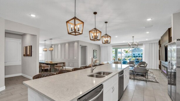 Une cuisine moderne dotée d’un grand îlot central, d’appareils électroménagers en acier inoxydable et de luminaires suspendus.