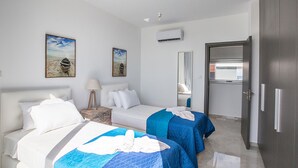 Een hotelkamer met twee bedden, een nachtkastje met een lamp, een spiegel, een airconditioningsunit en een deur.