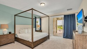 Un dormitorio con cama con dosel, una mesita de noche con lámpara, un aparador y un televisor en la pared.