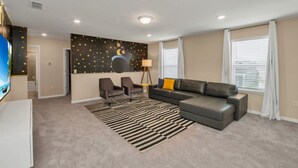 A modern living room with a sectional sofa, two armchairs, a black and white striped rug, a wall mural with stars and a crescent moon, and a floor lamp. - Your Family Will Love the 1st Class Amenities at Your Private Villa on Windsor Island Resort, Orlando Villa 5044 (Kissimmee)