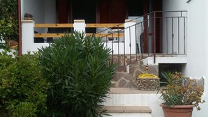 Una casa con entrada empedrada, escalera de madera y plantas en macetas.
