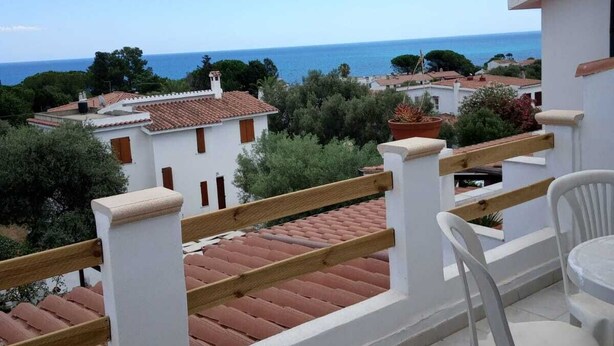 Un balcón con vista al mar, paredes blancas y tejados de tejas rojas.