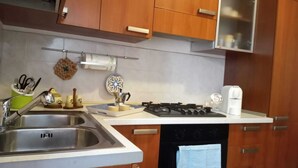 Una cocina con armarios de madera, un lavamanos de acero inoxidable, una estufa a gas y una cafetera.