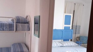 Una habitación con literas, un banco de madera y una cama con toallas ordenadas.