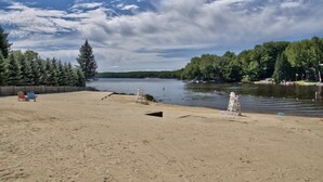 Una playa arenosa con un lago tranquilo, rodeada de árboles y una valla de madera.