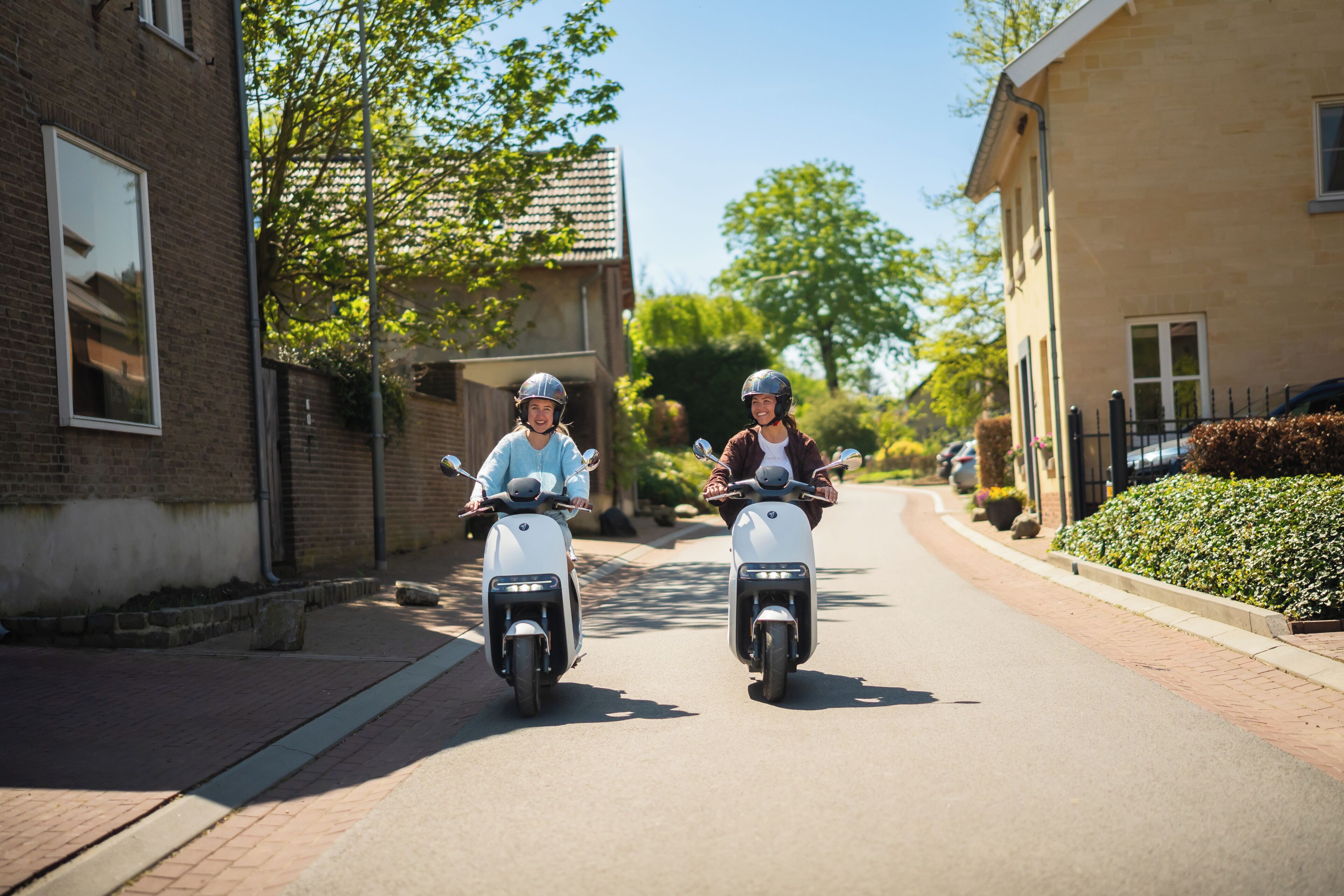 Deux personnes sur des scooters dans une rue résidentielle.
