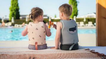 Two children sitting by a poolside with a clear view of the pool and lounge chairs in the background.