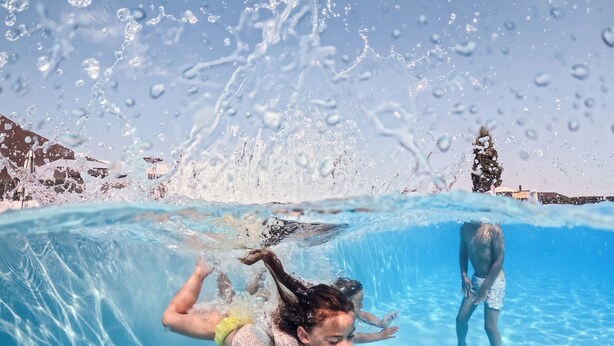 An underwater view of a swimming pool with clear water, a child swimming, and another person in the background.