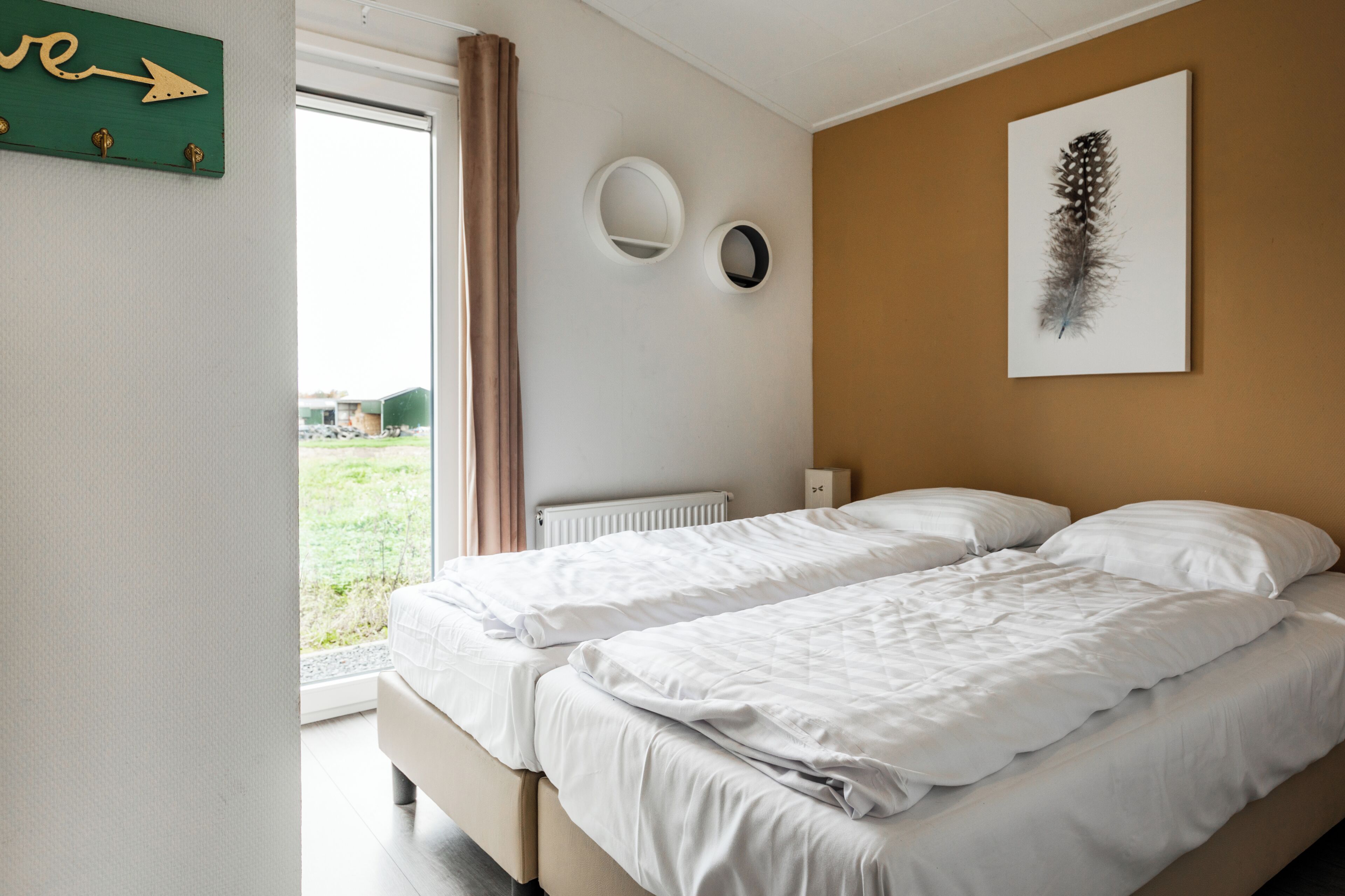 A bedroom with two beds, a window with curtains, a radiator, and a wall-mounted mirror.