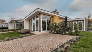 Ein modernes Haus mit einem Ziegelweg, der zu einem Eingang mit Glastür führt, umgeben von gepflegten Rasenflächen und Sträuchern.