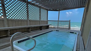 A wooden deck with a hot tub, wooden benches, and a view of the ocean.