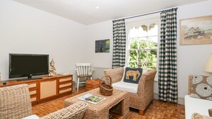 A cozy living room with wicker furniture, a flat-screen TV, and a window with checkered curtains.