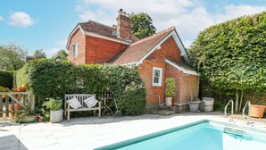 A house with a swimming pool, a wooden bench, and a garden with various plants.