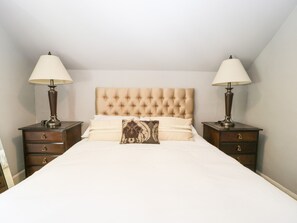 A neatly made bed with a tufted headboard, two bedside tables with lamps, and a small drawer unit under each table. - Downton Lodge (Lymington)
