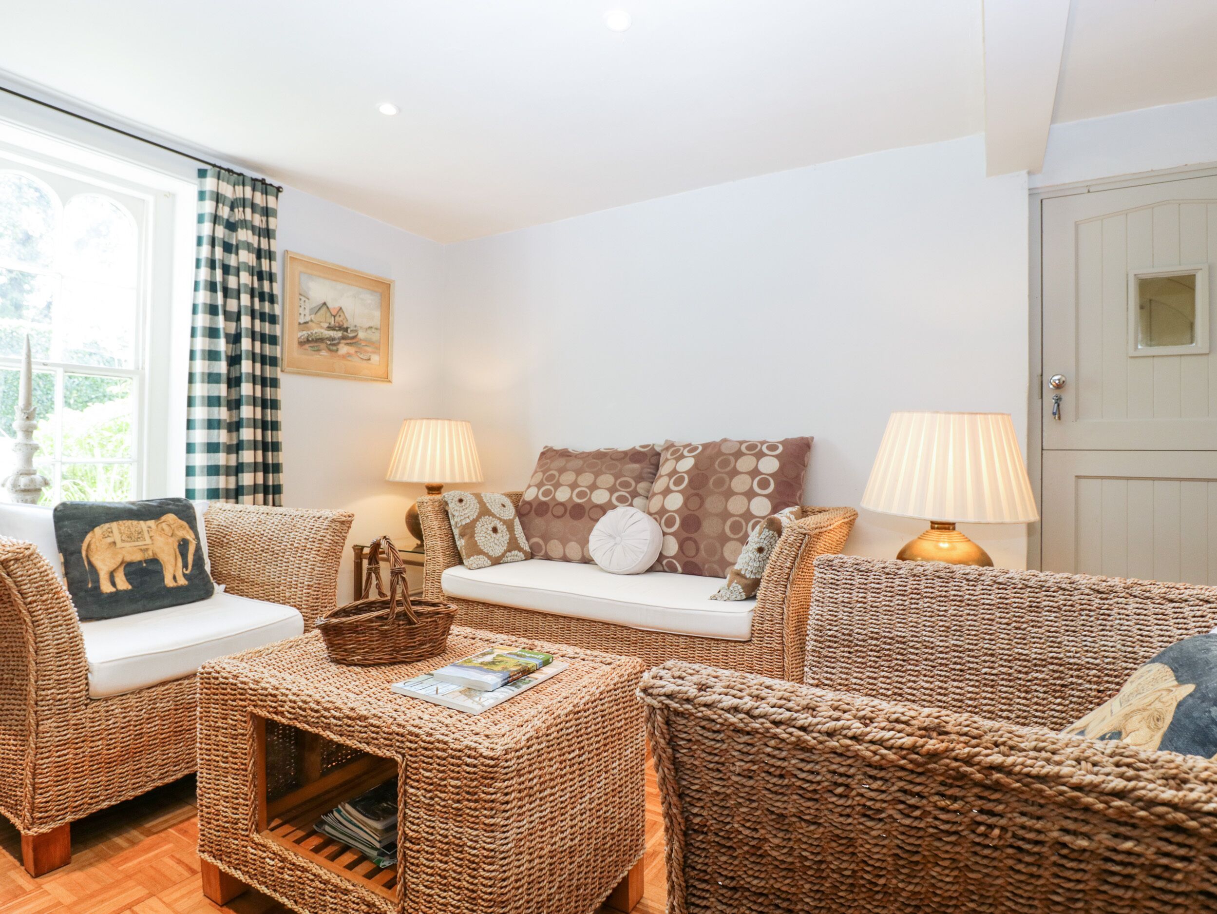 Una sala de estar acogedora con muebles de mimbre, un sofá blanco y dos lámparas.