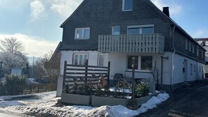 Een huis met twee verdiepingen, een balkon, schoorsteen en een hekwerk.