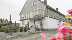 Een woonhuis met twee verdiepingen, een balkon, een voortuin en een kleine tuin.