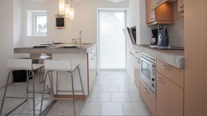 Een moderne keuken met een groot eiland, barstoelen, een inbouwoven en een koffieapparaat.