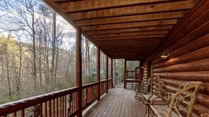Une cabane en bois dotée d’une véranda, de balustrades en bois et offrant une vue sur la forêt.