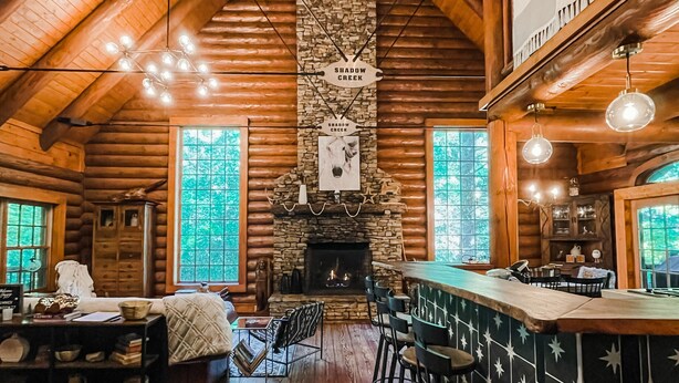 L’intérieur d’une cabane en rondins, avec une cheminée en pierre, des poutres en bois au plafond et un coin bar.