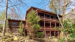 Une cabane rustique avec une façade en bois, un balcon et un foyer au premier plan.