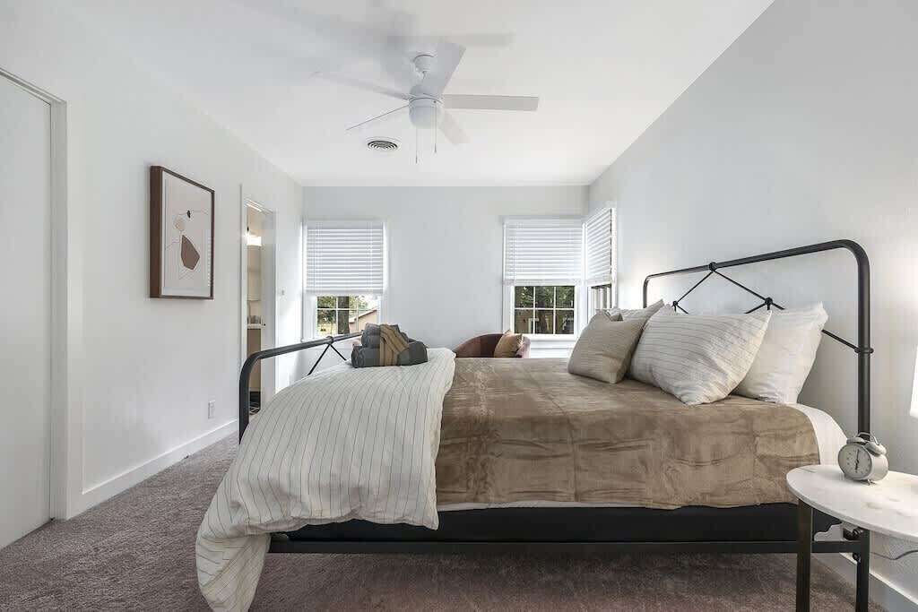 Une chambre à coucher comprenant un lit, un ventilateur de plafond, une table de chevet et une fenêtre avec des stores.