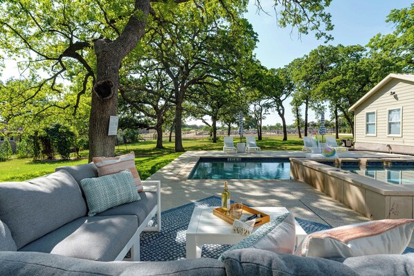 Ein Poolbereich mit einer Couch und Sesseln, einem kleinen Häuschen und einem großen Baum.