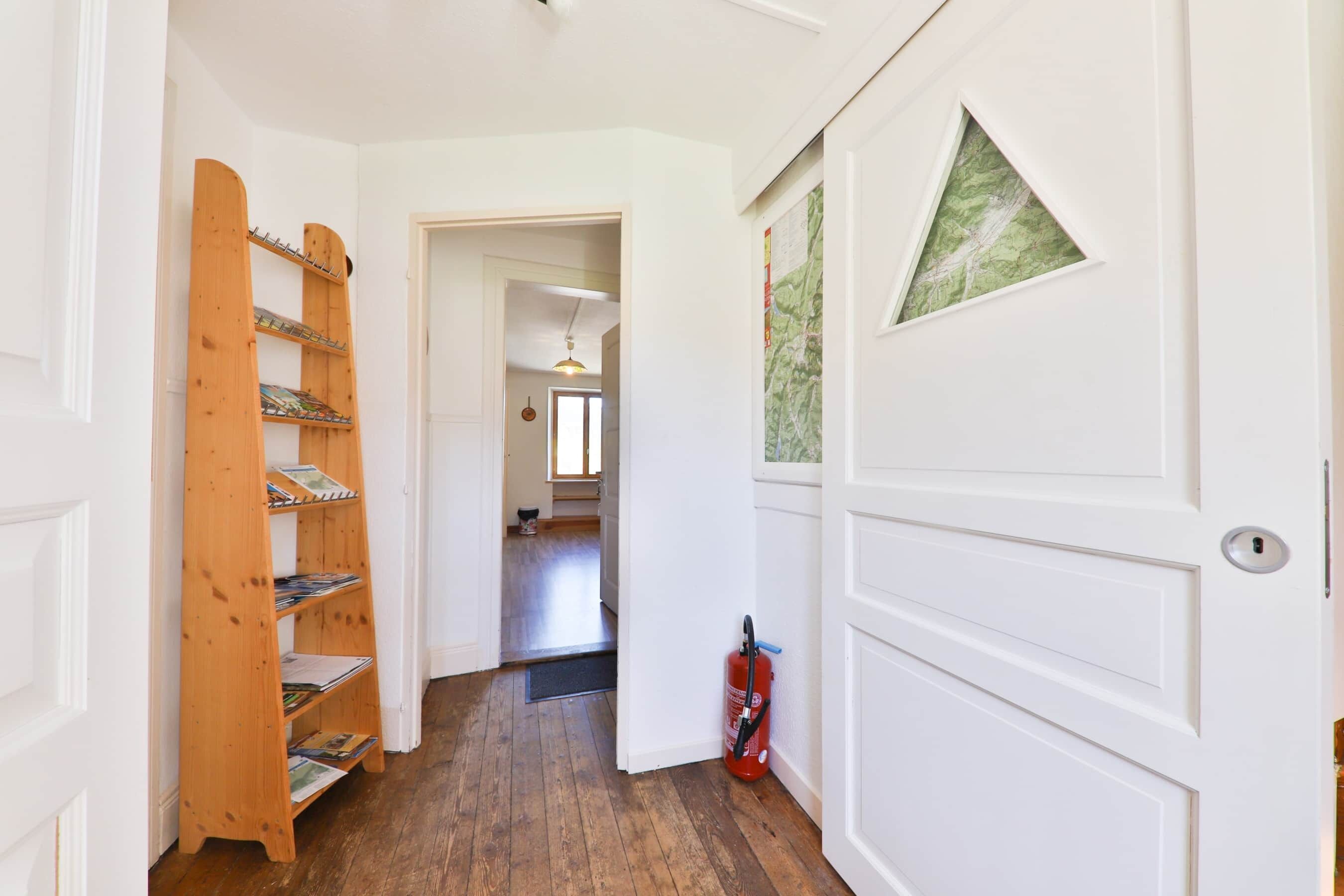 A hallway with a wooden shelf unit, a white door with a map, and a fire extinguisher.