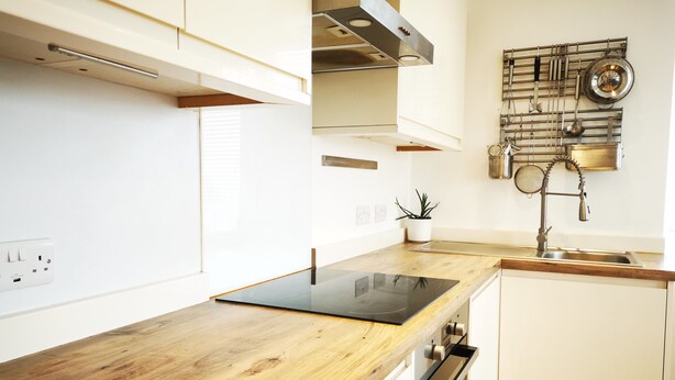 A modern kitchen with white cabinetry, a wooden countertop, a built-in oven, and a stainless steel sink.