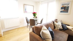 A living room with a brown sofa, a dining table with chairs, and a large window.