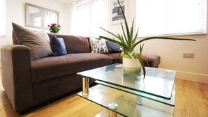 A modern living room with a brown sofa, a glass coffee table, and a potted plant.