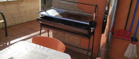 A patio with a grill, a table with a lace tablecloth, and orange chairs.