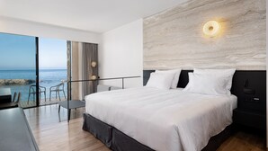 A modern bedroom with a large bed, a desk, and a view of the sea.
