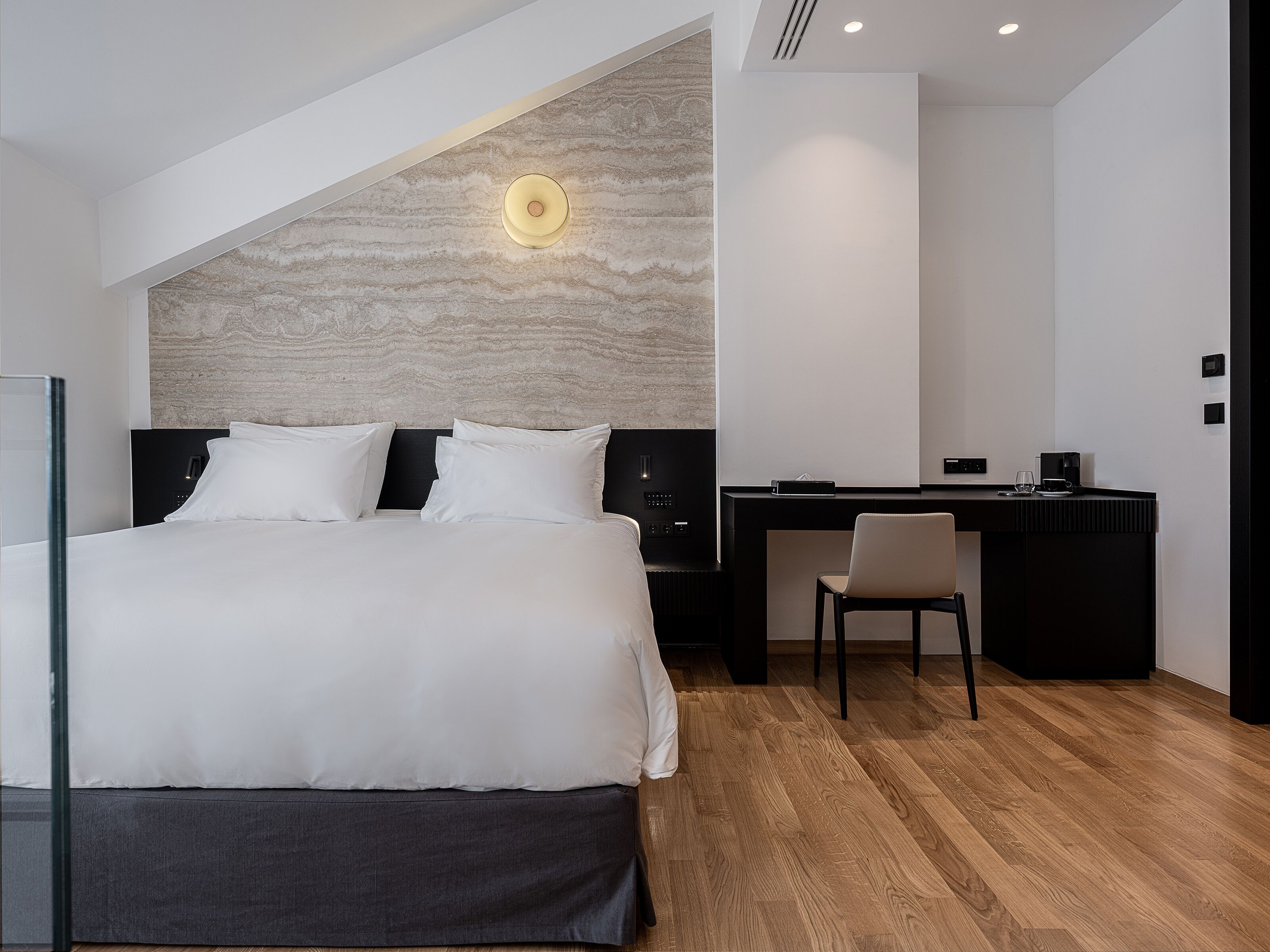 A modern hotel room with a large bed, a desk, and a chair.