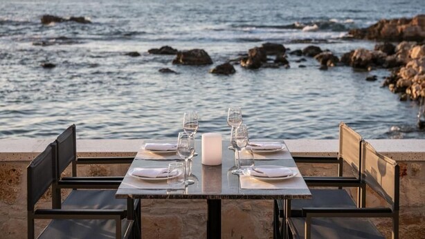 A table set for two with a view of the sea and rocks.