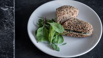 Un plato blanco con dos sándwiches y vegetales sobre una superficie de mármol oscuro.